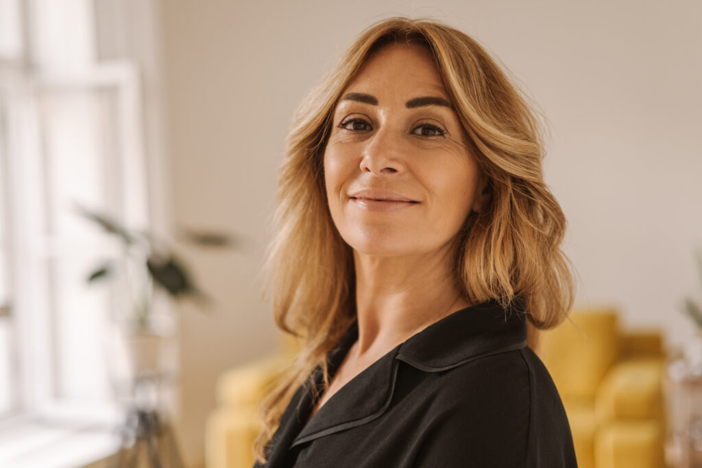 Close up of pretty middle aged caucasian lady in black shirt with smile on her face looks at camera.